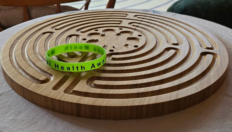 Green rubber bracelet with the words: Mental Health Awareness Month, resting on a wooden, finger labyrinth